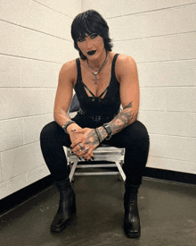 a woman is sitting on a stool with her hands folded