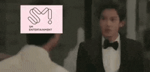 a man in a tuxedo is talking to another man in front of a pink sm entertainment logo .