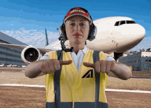 a woman wearing headphones and a yellow vest with the letter a on it stands in front of an airplane