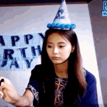 a woman wearing a birthday hat is writing on a piece of paper in front of a happy birthday sign .