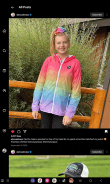 a girl in a rainbow jacket is standing in front of a fence