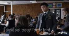 a boy in a school uniform is talking to a girl in a cafeteria while holding a tray of food .