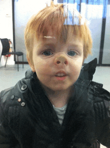 a young boy with red hair and blue eyes is wearing a black jacket with buttons on the sleeves