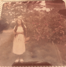 a woman in a white dress is standing in front of trees