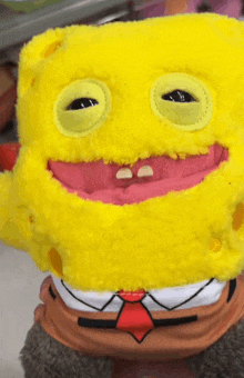 a yellow stuffed spongebob with a red tie and missing teeth