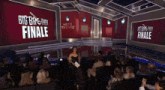 a woman stands on a stage in front of a large screen that says " live big brother finale "