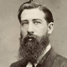 a black and white photo of a man with a beard in a suit and tie .