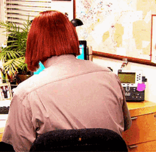 a woman with red hair is sitting at a desk with a telephone and a map on the wall behind her