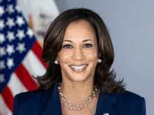 a woman wearing a pearl necklace and earrings is smiling in front of an american flag