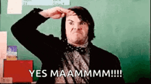 a man in a bow tie is saluting in front of a green chalkboard in a classroom .