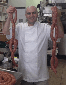 a man in a white chef 's coat holds a bunch of sausages