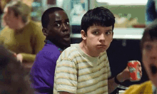 a group of young boys are sitting at a table in a restaurant . one of the boys is holding a soda can .