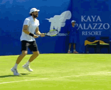 a man is holding a tennis racquet on a tennis court in front of a sign that says kaya palazzo resort