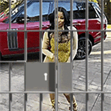 a woman is standing behind bars with a red suv in the background