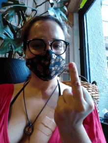 a woman wearing glasses and a face mask giving the middle finger