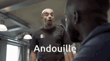 a man wearing a black shirt that says andouille stands next to another man