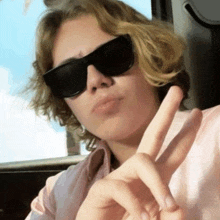 a young man wearing sunglasses is making a peace sign with his fingers .