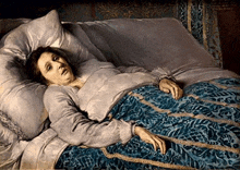 a woman is laying in a bed with a blue blanket