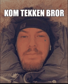 a man with a beard wearing a black hat and a jacket with the words kom tekken bror written on it