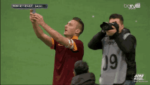 a soccer player takes a selfie while a cameraman takes a picture with the number 19 on his vest