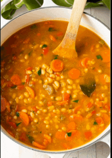 a pot of soup with carrots and beans is being stirred with a wooden spoon