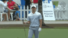 a man is holding a golf club on a golf course in front of a sign that says playground kids zone .