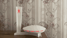 a white object with a red star on top of it is on a table in front of a floral wallpaper