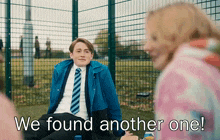 a boy in a blue jacket and tie sits in front of a fence with the words " we found another one " above him