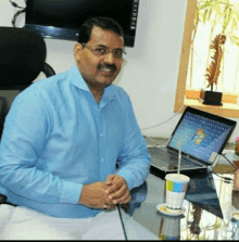 a man in a blue shirt sits at a desk with a laptop