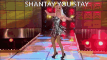 a woman in a silver dress is dancing on a stage with the words shantay you stay written above her