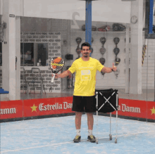 a man in a yellow shirt is holding a tennis racket in front of a estrella damm sign