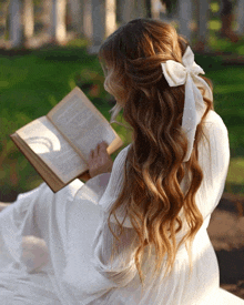 a woman in a white dress with a white bow in her hair is reading a book