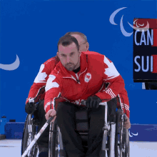 a man in a wheelchair holds a hockey stick in front of a sign that says " can sui "