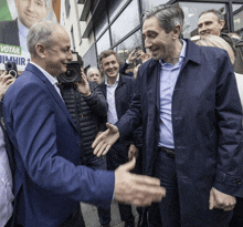 a man in a blue jacket shakes hands with another man in front of a votail sign