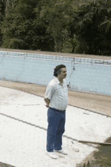 a man in a white shirt and blue jeans is standing in front of an empty swimming pool .