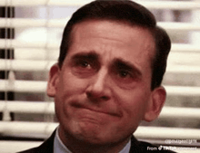 a man in a suit and tie is crying while sitting in front of a window .