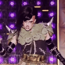 a drag queen is standing on a stage wearing a costume with spikes .