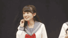 a girl in a school uniform with a red bow is smiling and eating something