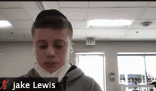 a young man wearing a mask looks at the camera with the name jake lewis on the bottom right