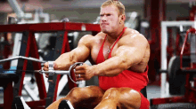 a man in a red tank top is using a rowing machine in a gym with the words building the body beautiful below him