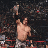 a man in a wrestling ring holds a championship belt over his head