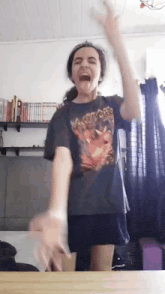a girl in a warriors shirt is standing in a living room with her hands in the air .