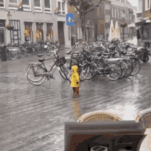 a little boy in a yellow raincoat is standing in the rain in front of a row of parked bikes .