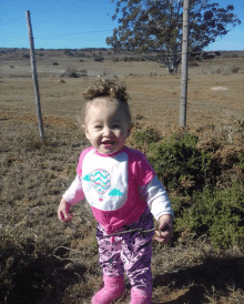 a little girl wearing a bib with a hot air balloon on it stands in a field