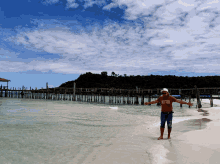 a man standing on a beach with his arms outstretched wearing a shirt that says ' hawaii ' on it