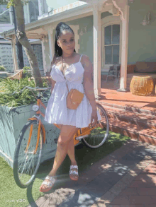 a woman in a white dress is standing next to an orange bicycle taken by a vivo y20