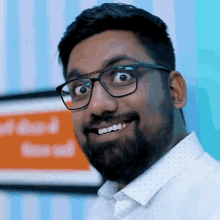 a man with glasses and a beard is smiling in front of an orange sign that says ' time out '