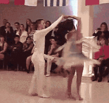 a man and a woman are dancing on a dance floor in front of a crowd with flags hanging from the ceiling