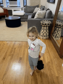 a little girl wearing a hello kitty shirt stands on a hardwood floor