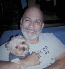 a man wearing a guess shirt holds a small dog